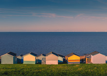 Colourful Beach Huts Along A Grass Verge In Tankerton, Whitstable, Kent, UK. The Sea And Sky Are Blue On A Sunny Winter Day, Late In The Afternoon. The Wind Farm Can Be Seen On The Horizon