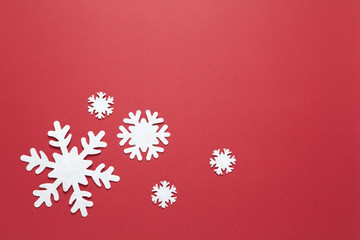 Christmas composition, group of big and small white felt snowflakes on burgundy red background, copy space. Festive, New Year concept. Horizontal, flat lay. Minimal style. Top view