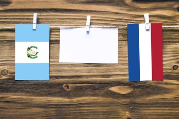 Poster - Hanging flags of Guatemala and Netherlands attached to rope with clothes pins with copy space on white note paper on wooden background.Diplomatic relations between countries.