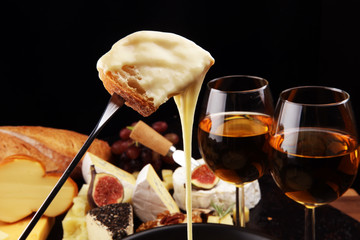 Gourmet Swiss fondue dinner on a winter evening with assorted cheeses on a board alongside a heated pot of cheese fondue with two forks dipping