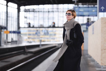 Mature Woman With Camera Wearing Black Coat And Large Wool Scarf Waiting At Platform
