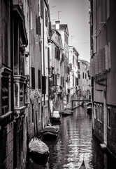 Wall Mural - Old houses with moored boats, Venice, Italy. Vertical view of narrow street in black and white. Vintage architecture of Venice in summer. Scenery of small canal in the Venice city.