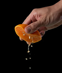 Wall Mural - hand squeeze orange slice with orange juice on black background