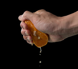 Wall Mural - hand squeeze orange slice with orange juice on black background