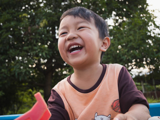 Asian child boy laughing with happy close up face outdoor with natural background. Family relax and freedom time in summer holiday. Young kid smile while playing outdoor.