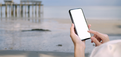 Wall Mural - Young female holding blank screen smartphone with beach background