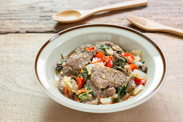 close up of stir fried beef with basil in a ceramic dish on wooden table. hot and spicy thai style food menu.