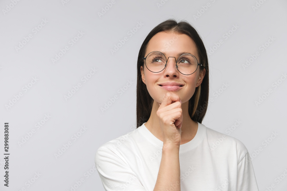 Portrait of young woman with dreamy cheerful expression, thinking, wearing glasses, isolated on gray background with copy space - obrazy, fototapety, plakaty 