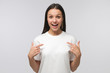 © Damir Khabirov - Young surprised woman pointing to her white tshirt with fingers, showing empty space for your text, isolated on gray background