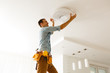 © Angelov - Electrician is installing and connecting a lamp to a ceiling.