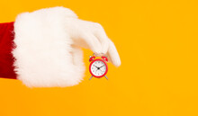 Santa Hand Holding Small Red Alarm Clock With Time On Orange