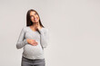 © Prostock-studio - Happy Pregnant Woman Thinking Standing Over Gray Studio Background