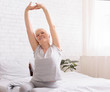 Well-slept senior lady stretching with arms raised in bed