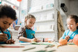 © pressmaster - Two cute diligent girls and African boy drawing with highlighters by desk