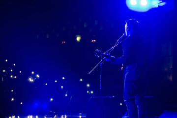 Wall Mural - A young man with guitar sings in front of a hall full of lights and flashes