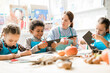 © pressmaster - Multiracial schoolkids and teacher in aprons cutting out halloween decorations