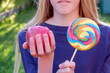 Teenage blonde caucasian girl in blue top choosing between junk food lolly and healthy apple. Healthy clean detox eating concept.