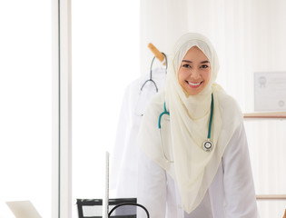 Portrait of charming muslim female doctor working at office desk and smiling at camera.