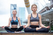 © iammotos - two beautiful sport women doing yoga asana on mat in urban city outdoors . group of female people wearing sportswear practicing meditation in Lotus pose . fitness Healthy lifestyle concept . workout