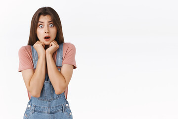 Wall Mural - Shocked, scared timid insecure cute girl in dungarees and t-shirt, frightened staring camera feel unsafe and horrified from shocking news, shivering, press hands to chest terrified