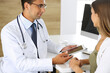 © Iryna - Doctor and patient discussing medical exam results while sitting at the desk in clinic. Male physician using tablet computer for filling up medication history records of young woman. Data in medicine