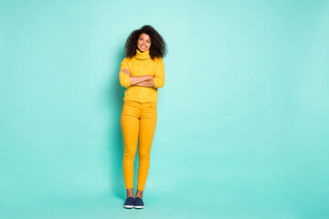 Full length photo of amazing dark skin lady holding arms crossed looking wondered empty space wear yellow knitted pullover trousers isolated blue teal color background