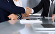 © Iryna - Business people shaking hands after contract signing at the glass desk in modern office. Unknown businessman with colleagues at meeting or negotiation. Teamwork, partnership and handshake concept