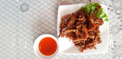 Wall Mural - Top view or Flat lay of Fried sun dried pork and green cabbage leaves in white plate with small bowl of hot chili sauce on dining table with copy space 