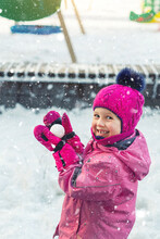 Cute Adorable Caucasian Little Girl Winter Portrait Holding Snowball In Hands Ready For Snow Fight At Playground Outdoor. Funny Playful Child During Snowfall At Cold Season Outside. Happy Childhood