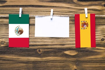 Wall Mural - Hanging flags of Mexico and Spain attached to rope with clothes pins with copy space on white note paper on wooden background.Diplomatic relations between countries.