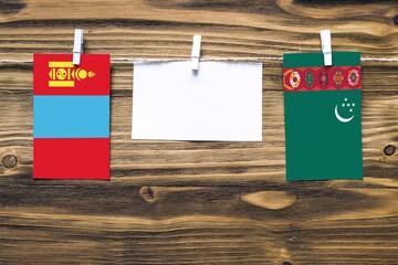 Hanging flags of Mongolia and Turkmenistan attached to rope with clothes pins with copy space on white note paper on wooden background.Diplomatic relations between countries.