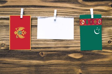 Hanging flags of Montenegro and Turkmenistan attached to rope with clothes pins with copy space on white note paper on wooden background.Diplomatic relations between countries.