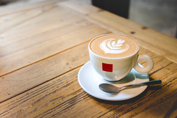 Coffee latte art in a white coffee cup and coffee spoon on wooden background, breakfast morning concept in a cafe, with vintage style effect, close up with copy space