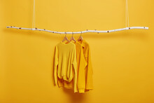 Selective Focus. Three Items Of Clothes On Hangers. Long Sleeved Yellow Jumpers On Wooden Rack Near Bright Vivid Wall. Copy Space For Text. Various Casual Outfits Hanging In Row At Dressing Room