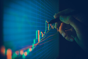 Closeup hand pointing pen on blue color monitor to analyze stock market graph