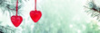 Two red hearts glass decorations on pine branch covered with snow, banner with green background and space for text. Love, Christmas, New Year or Saint Valentine concept