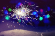 Christmas or New year sparkler Bengal light on snow, dark background with blurred multicolored lights