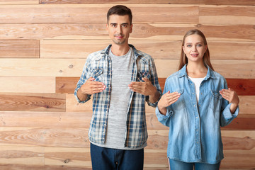 Wall Mural - Young deaf mute couple using sign language on wooden background