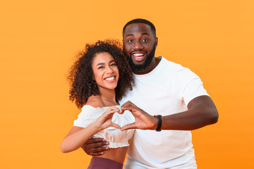 Wall Mural - Portrait of happy African-American couple making heart with their hands on color background