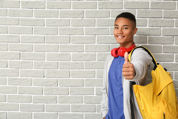 Portrait of African-American teenage schoolboy showing thumb-up on brick background