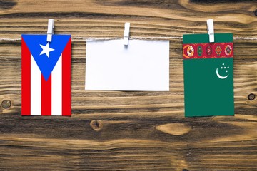 Hanging flags of Puerto Rico and Turkmenistan attached to rope with clothes pins with copy space on white note paper on wooden background.Diplomatic relations between countries.