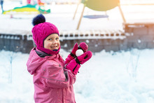 Cute Adorable Caucasian Little Girl Winter Portrait Holding Snowball In Hands Ready For Snow Fight At Playground Outdoor. Funny Playful Child During Snowfall At Cold Season Outside. Happy Childhood