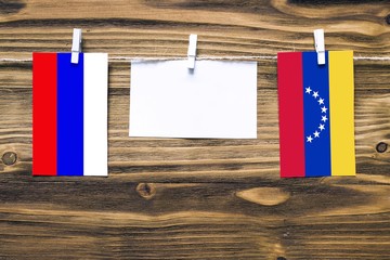 Wall Mural - Hanging flags of Russia and Venezuela attached to rope with clothes pins with copy space on white note paper on wooden background.Diplomatic relations between countries.