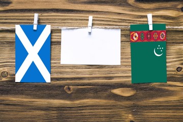 Hanging flags of Scotland and Turkmenistan attached to rope with clothes pins with copy space on white note paper on wooden background.Diplomatic relations between countries.