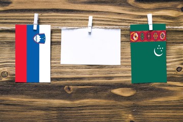 Hanging flags of Slovenia and Turkmenistan attached to rope with clothes pins with copy space on white note paper on wooden background.Diplomatic relations between countries.
