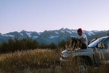 Man Sitting On Hood Of The Truck In Alaskan Mountains During Sunset