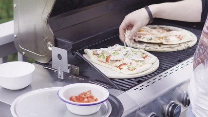 Canvas Print - Preparing individual grilled pizzas on an outdoor gas grill.