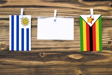 Wall Mural - Hanging flags of Uruguay and Zimbabwe attached to rope with clothes pins with copy space on white note paper on wooden background.Diplomatic relations between countries.
