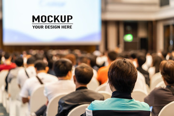 rear view of audience listening speakers on the stage with presentation via projector in the confere