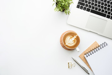 White minimalist office desk table with laptoo computer, notebooks with pen, cup of latte coffee and supplies. Top view with copy space, flat lay.